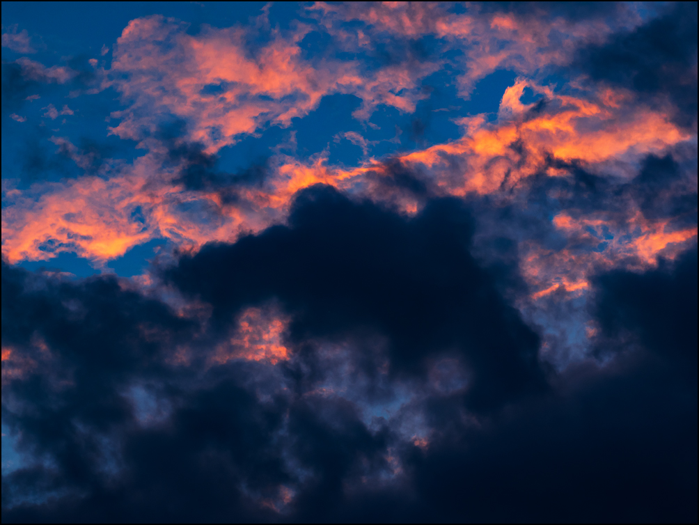 An abstract photograph of orange clouds behind dark clouds in the early morning sky over Fort Wayne, Indiana.