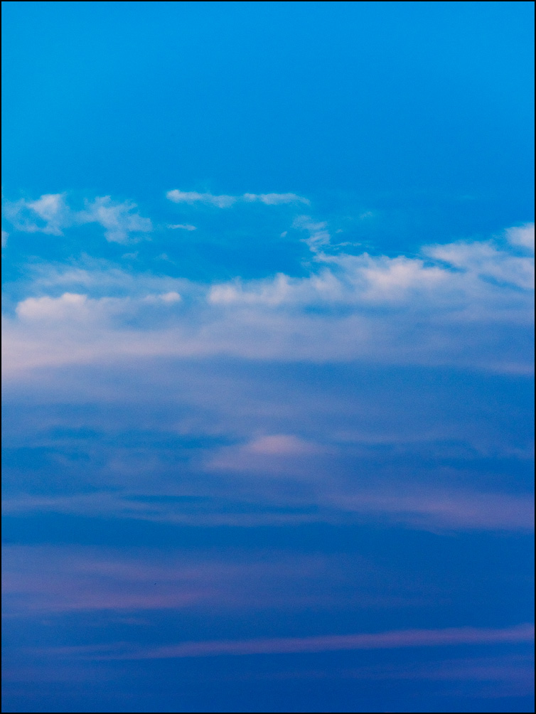 An abstract photograph of white and purple clouds in the blue sky shortly before sunset.