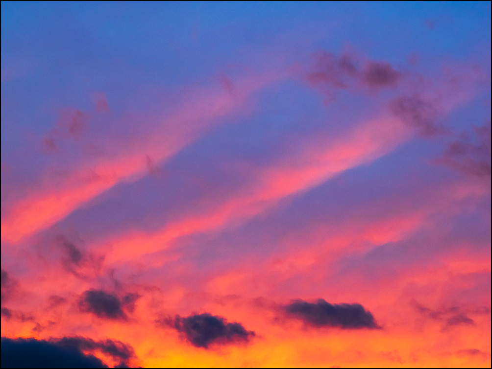 An abstract photograph of diagonal lines of red clouds in a dark sky at sunset on an August evening in Indiana.