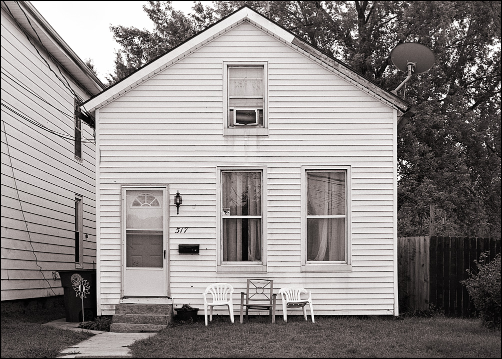 A small white house with three plastic lawn chairs in the yard on High Street in Fort Wayne, Indiana.