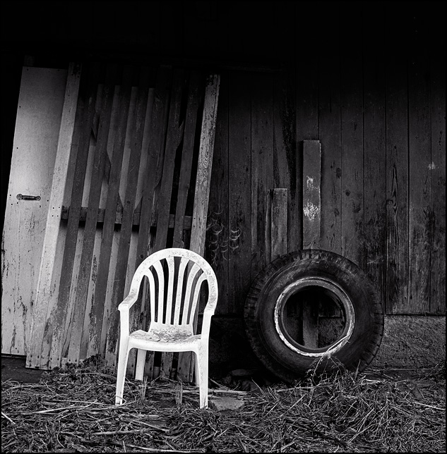 A plastic patio chair and an old tractor tire next to an abandoned barn in Indiana.