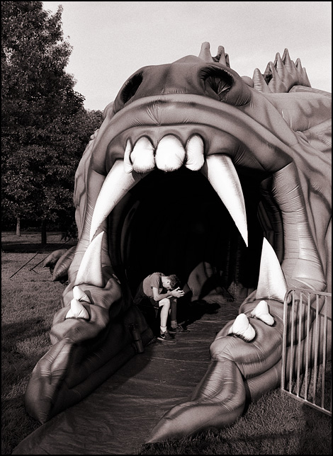 A carnival worker sitting inside the open mouth of a giant inflatable dragon called The Beast.