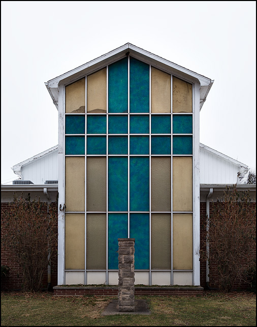 Colored glass windows form a giant blue cross on a yellow background on the end of Benton Mennonite Church in the small town of Benton, Indiana.