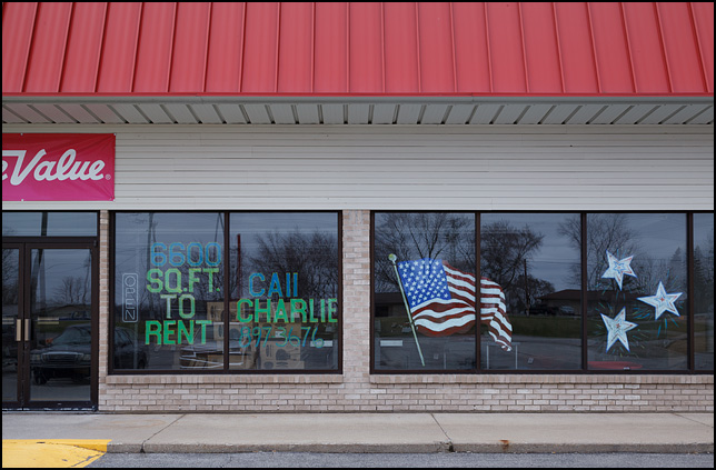 An American flag and stars painted on the front windows of a vacant storefront for rent in Avilla, Indiana.