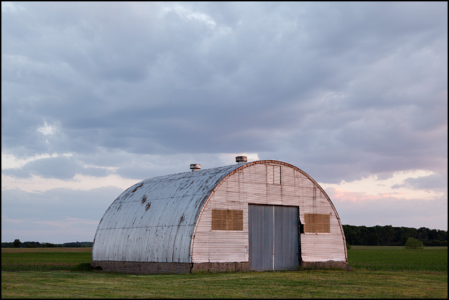 A quonset hut used as a barn sits in a field at sunset on County Road 1200N in rural Wells County, Indiana.