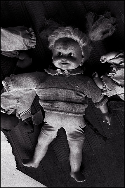 An old Cricket talking doll on the floor of an abandoned house surrounded by a Cabbage Patch Kid and a headless doll baby.