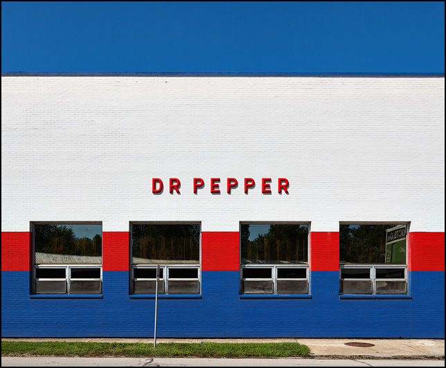 A Dr. Pepper sign on the side of the Pepsi distribution center on Harrison Street in Fort Wayne, Indiana. The brick building is painted red, white, and blue.