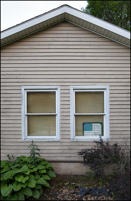 A faded American flag sign with God Bless America written on it hangs in the front window of a small house in Fort Wayne, Indiana.