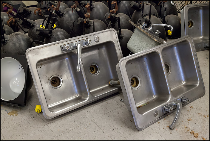 Several stainless steel sinks and faucets lay on the floor in front of a bunch of stage lights from the school auditorium during the pre-demolition sale held at Elmhurst High School on January 27, 2018.