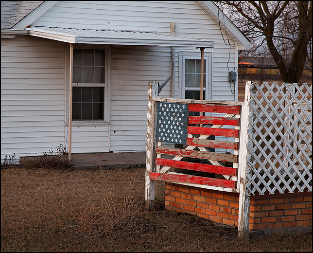 An American Flag painted on a weathered wood fence in front of an old house on Lafayette Center Road in rural Allen County, Indiana.