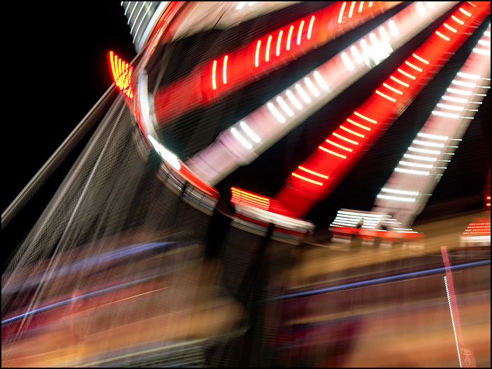 The Flying Circus ride, a swing carousel, photographed in motion at night at the 2019 Three Rivers Festival carnival in Fort Wayne, Indiana. The photo is a blur of light and color.