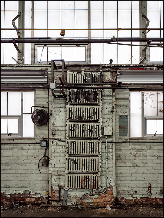 Steam heat radiators on the wall between the windows in Building 22 at the abandoned General Electric factory complex on Broadway in Fort Wayne, Indiana.