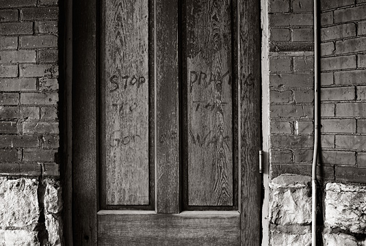 An old door with graffiti that says Stop Praying to the god of war.