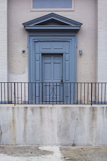 The front door of an abandoned brick bank building on Third Street in Louisville, Kentucky. The door is an ornate federal style door with wrought-iron railing around the entrance.