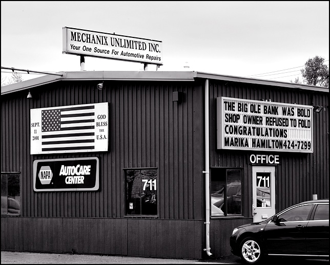 Mechanix Unlimited auto repair has signs with an American flag commemorating the 9-11 attacks and a sign condemning a bank for trying to foreclose on a local small business.