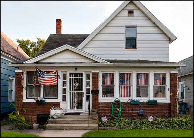 An old house with five American flags in the windows of the screened in porch. The house is on 6th Street in the small city of Mishawaka, Indiana.
