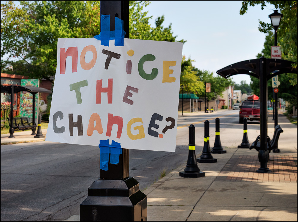 A handmade sign with colorful letters taped to a light pole on Wells Street in Fort Wayne, Indiana. The sign says, Notice The Change?