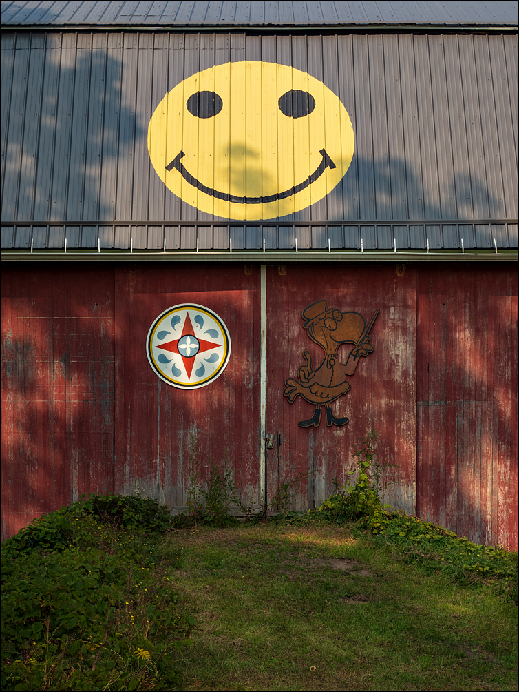 A red barn with a big yellow smiley face painted on the roof on State Road 31 in rural Monroe County, New York.