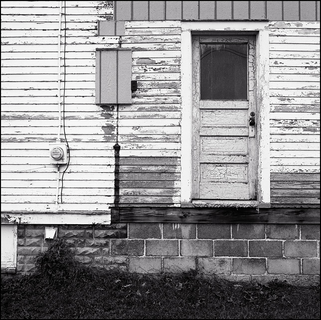 A door with no stairs hovers above the ground on the back on an abandoned house.