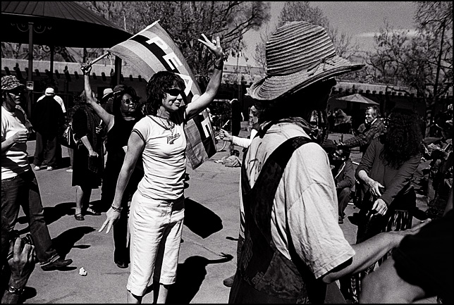 A peace activist waves a rainbow peace flag while people dance around her at an antiwar rally on the anniversary of the Iraq War in the Santa Fe Plaza.