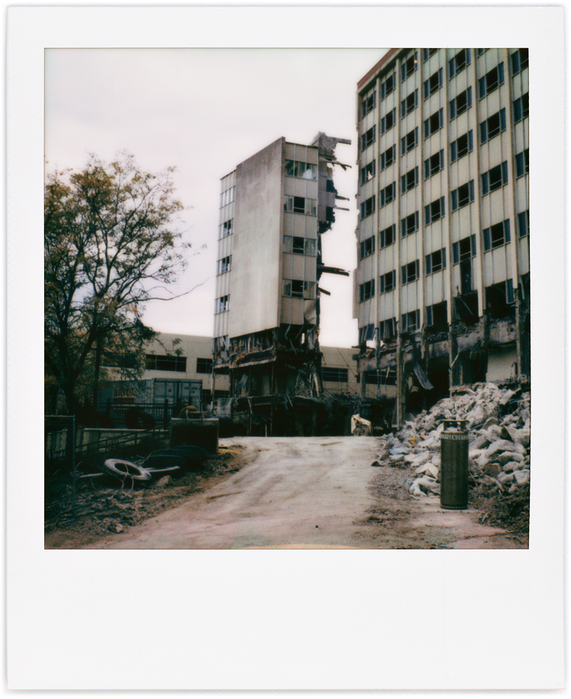 A Polaroid photo of the front of Saint Joseph Hospital in downtown Fort Wayne, Indiana. One section of the building has been detached from the rest during the demolition of the hospital, making a freestanding tower next to the rest of the building.
