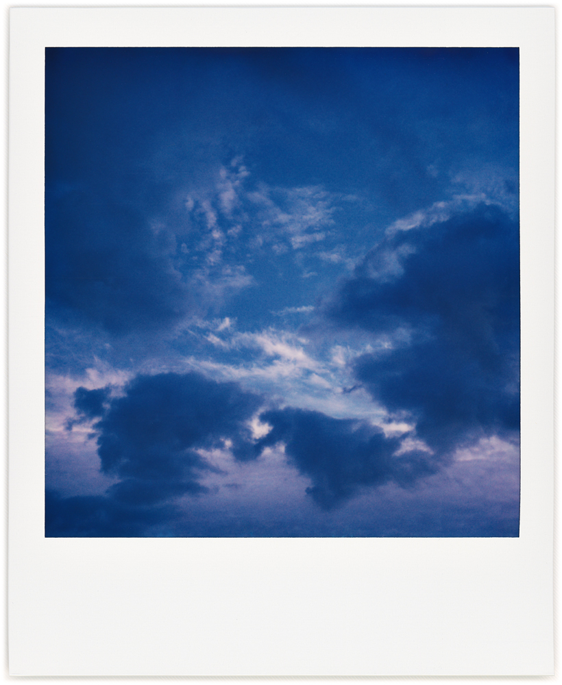 Polaroid abstract photograph of dark clouds around an area of blue sky mottled with smaller white clouds in the morning sky.