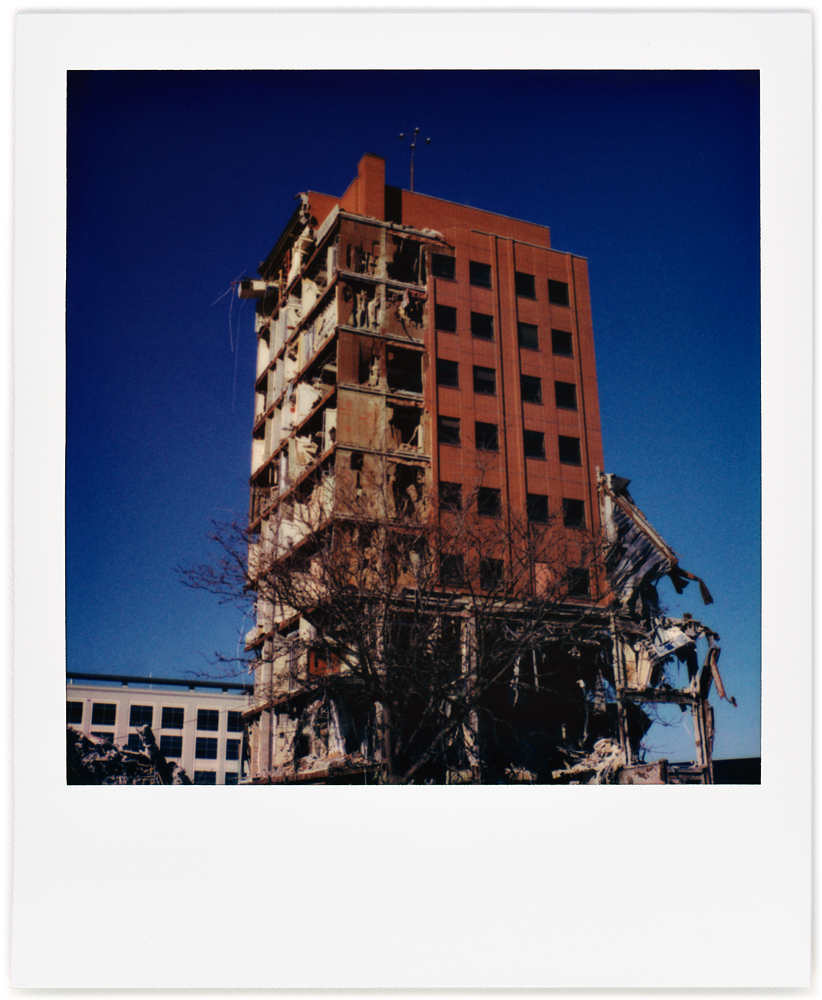 A Polaroid photo of a precarious broken tower of brick and steel beams, the last remaining section of the partially demolished Saint Joseph Hospital in downtown Fort Wayne, Indiana. The brick walls have been broken away from the lower floors.
