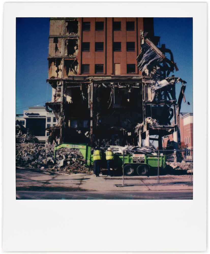 A Polaroid photo of the Saint Joseph Hospital demolition site in downtown Fort Wayne, Indiana. Two workers are standing in front of the small part of the building that still stands.