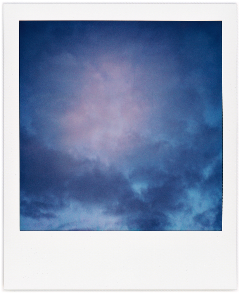 Polaroid abstract photograph of a V-shaped dark cloud formation with a round red cloud above it in the morning sky after sunrise.