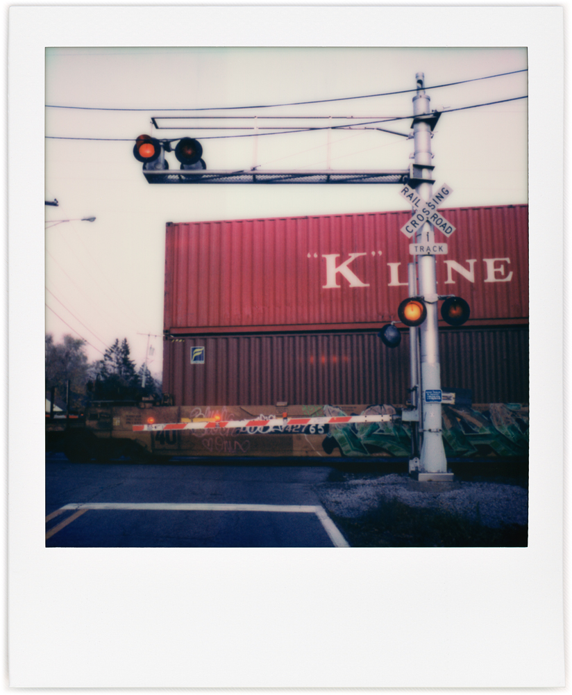 Polaroid snapshot of a train stopped on the Sandpoint Road railroad crossing in Fort Wayne, Indiana. Photographed late in the evening at sunset.