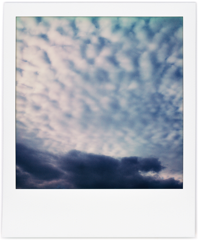 Polaroid abstract photograph of round white clouds radiating upward from a dark band of clouds.
