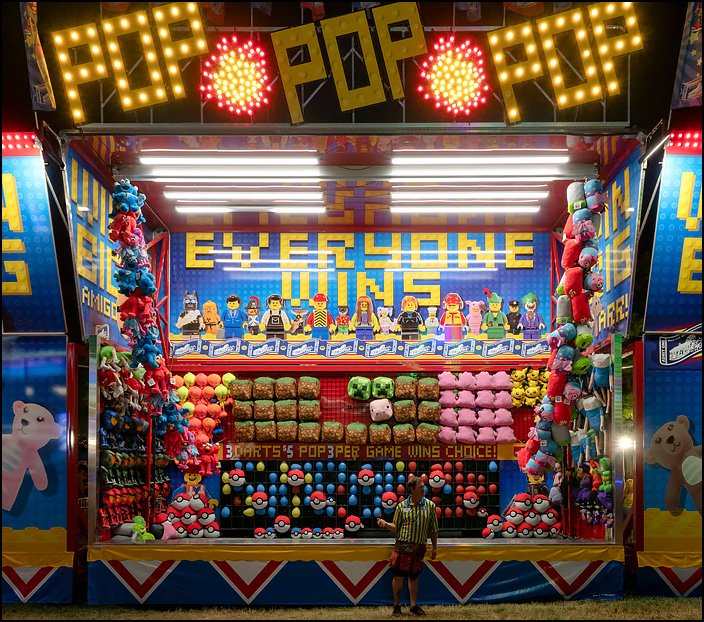 Pop Pop Pop is a carnival game where you throw a dart at balloons. The signs say that Everyone Wins, but no one is playing, leaving the carnival worker looking bored and lonely. 2019 Three Rivers Festival in Fort Wayne, Indiana.