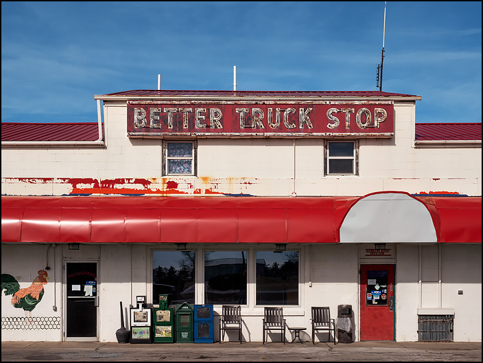 Ramblers Roost Truck Stop on Lincoln Highway in rural Van Wert County, Ohio. A large neon sign near the top of the old white cement block building says, Better Truck Stop.