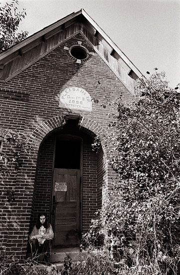 Self portrait of fine art photographer Christopher Crawford sitting in the front door of an abandoned one-room brick schoolhouse.