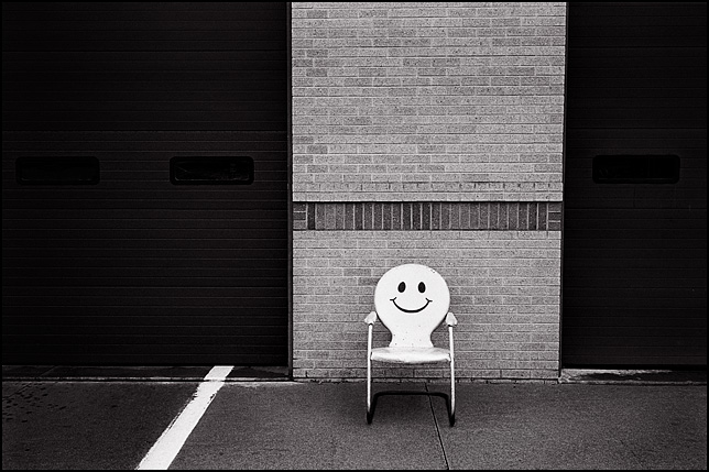 A metal motel chair with a smiley face painted on the back rest sits in front of Fire Station 10 at the corner of Crescent and Anthony in Fort Wayne, Indiana.
