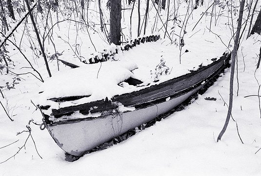 Snow covers an old wooden rowboat in the forest during the winter.