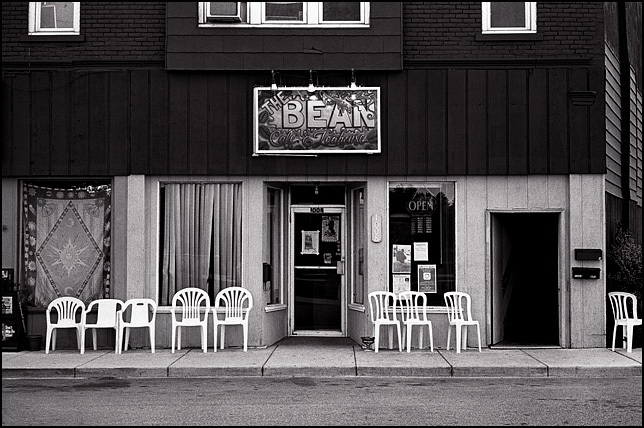 A row of plastic chairs on the sidewalk flanking the entrance to The Bean Coffee Shop on Wells Street in Fort Wayne, Indiana.