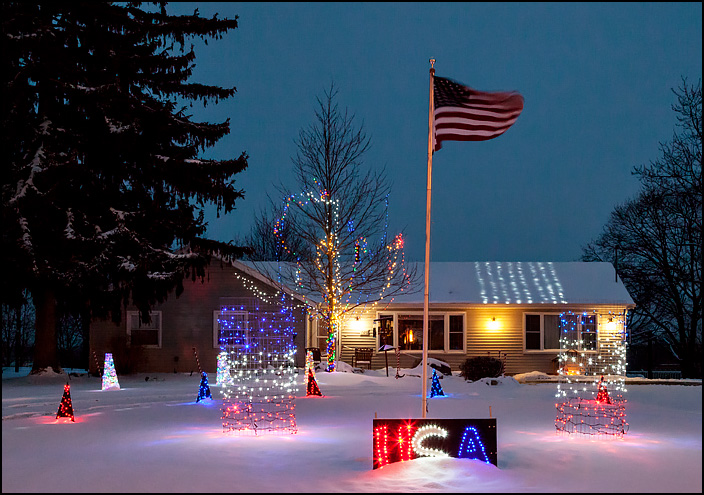 Patriotic Christmas lights in front of Dougs Sport Cuts, a barbershop in a house on Getz Road in Fort Wayne, Indiana. Red white and blue lights and a lighted USA sign. Photographed early in the morning just before dawn.