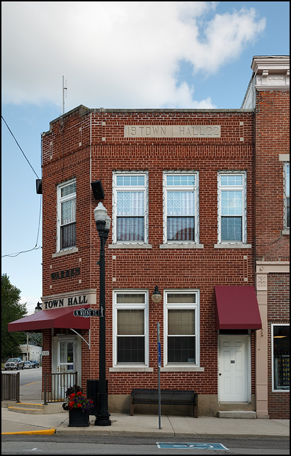 The two-story brick Town Hall building in the small town of Warren, Indiana. American flags hang over the top floor windows like patriotic curtains.