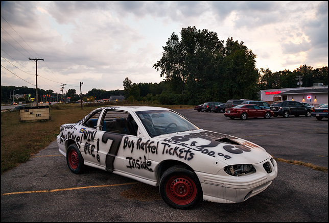 An old beat-up Pontiac Grand-Am spray-painted as a race car. It also has Win this car in a raffle painted all over it.
