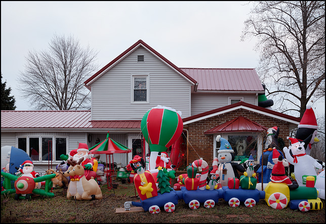 Inflatable Christmas decorations cover the front yard of a house on Main Street in the small town of Wolf Lake, Indiana. The decorations include Santa in an airplane, Santa in a hot air balloon, Santa in his sleigh, and Santa driving a train.