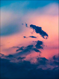 Abstract photograph of dark clouds in front of an orange and blue sky at sunset.